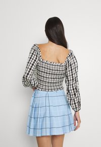 Haut à manches ballons à carreaux noir et blanc associé à une jupe plissée bleu clair avec un motif à carreaux. Texture douce, coupe structurée.