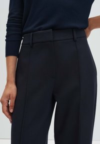 Pantalon sur mesure bleu marine à la texture lisse. Taille haute, poches latérales et coutures discrètes créent une apparence élégante.