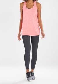 Top a canotta rosa melangiato con scollo rotondo, abbinato a leggings grigio scuro solidi e scarpe sportive grigie con accenti neri.