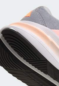 Primer plano de una suela de zapatilla gris y rosa con textura de goma negra y la marca "Cloudfoam" en la entresuela blanca.