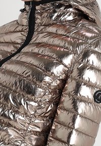 Giacca puffer oro rosa metallico con pannelli trapuntati verticali, colletto alto e zip nera, con una patch del logo sulla manica.