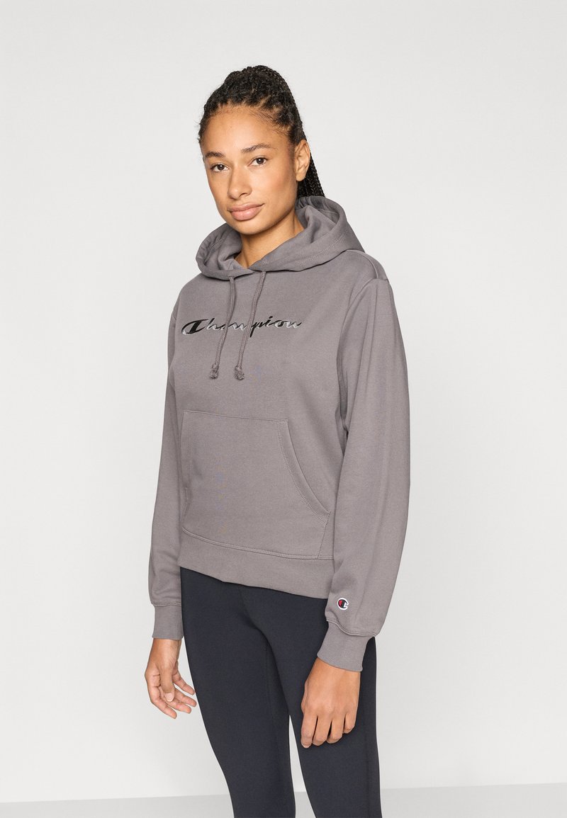 Γκρι φούτερ με τσαμπουράκια, μπροστινή τσέπη και λογότυπο "Champion". Ριμπ μανσέτες και τελείωμα, κατασκευασμένο από απαλό ύφασμα. Φορεμένο με μαύρο κολάν.