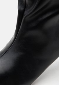 Gros plan d'une botte en cuir noir lisse avec des plis doux et une texture fine visible à la surface.