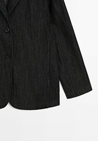 Blazer en denim noir avec un design structuré, une fermeture à un bouton et un tissu texturé avec des motifs de tissage visibles.