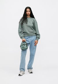 Zöld crewneck pulóver, vertikális csíkos farmerral, egy kicsi zöld táskával a kézben. Szürke részletekkel ellátott sneaker. Egyszerű, hétköznapi szett.