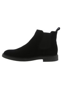 Bottines Chelsea en cuir suédé noir avec des panneaux latéraux élastiques, bout rond et languette pour un enfilage facile. Semelle en caoutchouc plate avec une adhérence minimale.