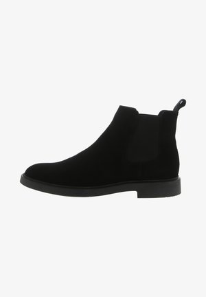 Zwarte suede Chelsea-boot met elastische zijpanelen, ronde neus en een lusje voor eenvoudig aan- en uittrekken. Platte rubberen zool met minimale profiel.