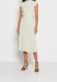 Ljusgrön knä-lång klänning med korta ärmar, instoppad midja och mjukt tyg. Buren med svarta remsandaler med genomskinlig klack.