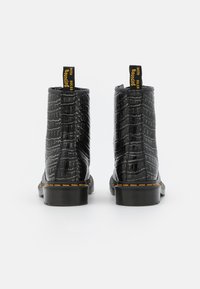 Botine din piele neagră, până la glezna, cu textură de crocodil, dotate cu accente galbene și o talpă groasă din cauciuc. Proiectate cu un tab pentru a fi îmbrăcate ușor.