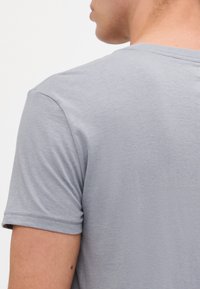 T-shirt gris à manches courtes en coton doux, avec col rond et texture lisse. Détails de couture minimal autour des manches.