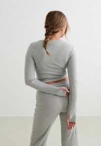 Maglietta grigia a maniche lunghe con un design aderente, texture a coste e una sezione ritagliata in vita, abbinata a pantaloni coordinati.