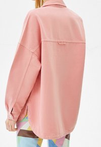Ljusrosa oversized skjorta med knappar och långärmar samt en bakre ögla. Tyget verkar mjukt med en avslappnad passform och sidoklipp.