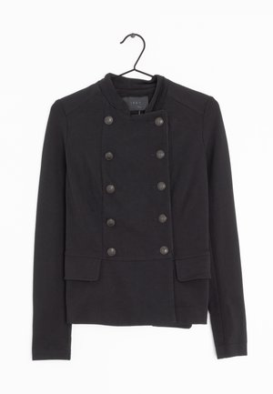 Veste noire croisée avec col rond et huit boutons, manches longues, et deux poches à rabat devant, suspendue sur un cintre noir.