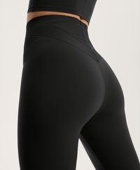 Crne legging hlače visokog struka od glatkog, rastezljivog materijala s nagibnim teksturama na pojasu, prilagođenim krojem i bešavnom dizajnom.