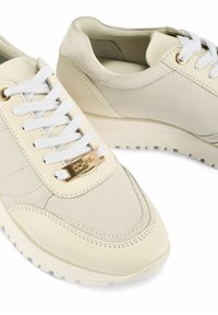 Jasno beżowe skórzane trampki z białymi sznurówkami, złotą płytką z logo, teksturowaną gumową podeszwą oraz gładkim, zaokrąglonym czubkiem.