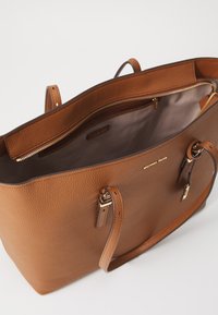 Sac fourre-tout en cuir brun à texture galet avec des doubles poignées supérieures, des accessoires en métal doré, et un intérieur spacieux comprenant une poche zippée et une doublure lisse.