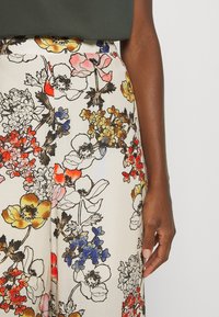 Pantalons larges fleuris en tissu crème. Présente des fleurs colorées en rouge, jaune, rose et bleu avec une texture lisse et une taille haute.