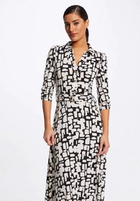 Schwarz-weiß gemustertes Kleid mit Kragen, Dreiviertelärmel, einem Gürtel mit runder Schnalle und einer Knopfverschluss vorne.