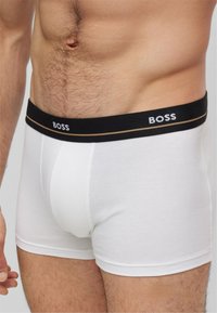 Boxer ajustados de algodón blanco con una banda elástica negra que presenta el nombre de la marca "BOSS" en blanco. Diseño simple, forma ajustada.