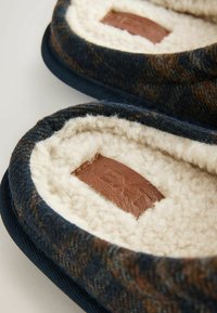Brune og blå mønstrede hjemmesko med en blød pelsforing, nubuck-detaljer og en polstret, rund form.