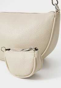 Beige leather handbag with a textured finish and a curved shape, accompanied by a small matching pouch with a zipper closure.