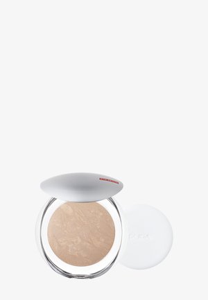 Cipria compatta in una confezione trasparente con coperchio argentato. La polvere beige presenta una texture marmorizzata. Include un disco applicatore bianco separato.