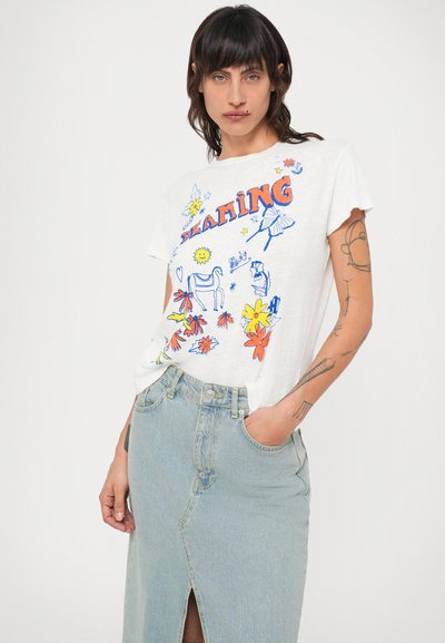 Tricou din bumbac, alb, cu un design grafic colorat care include flori și un unicorn. Asortat cu o fustă din denim bleu deschis, cu o fanta.