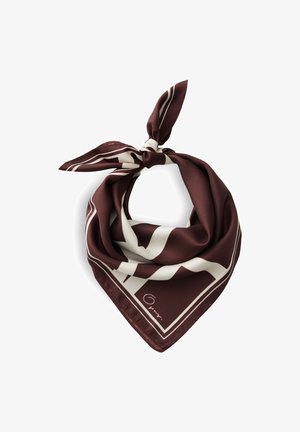 Femme aux cheveux courts et bruns porte une veste foncée et une écharpe bordeaux et blanche à motifs autour du cou, regardant légèrement sur le côté.
