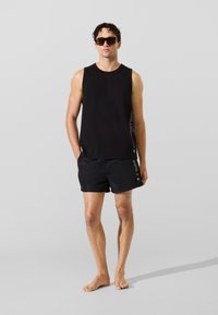 Juodas be rankovių viršus ir atitinkantys šortai, pagaminti iš lengvos medžiagos. Šortai turi logotipą ir yra skirti aktyviam gyvenimo būdui.