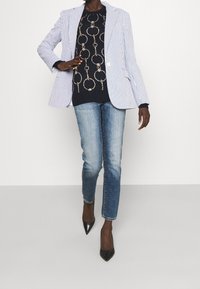 Pruhované sako, tmavě modrý svetr se vzorem, modré džíny a černé špičaté podpatky. Sako má na míru ušitý design se dvěma knoflíky a klopami.