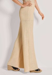 Beige gebreide uitlopende broek met een textuurpatroon. Het ontwerp heeft een hoge taille en wordt gecombineerd met zwarte sleehakken.