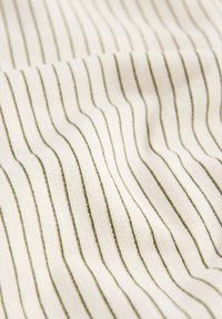 Tissu blanc avec de fines rayures verticales vert foncé et texture côtelée visible créant des plis doux.
