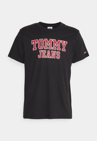 Juodas medvilnės marškinėliai su raudonais ir baltais "TOMMY JEANS" užrašais priekyje. Trumpomis rankovėmis ir apvalia kaklo iškirpte. Lygi tekstūra.