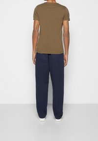 Oliivinvihreä lyhythihainen T-paita pyöreällä kaula-aukolla, yhdistetty löysälahkeisiin tummansinisiin housuihin ja valkoisiin lenkkareihin. Yksivärinen pinta, ei kuvioita.