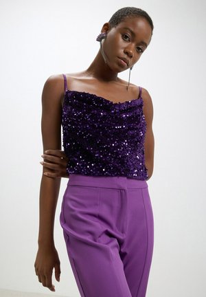 Top viola con paillettes e scollatura drappeggiata, abbinato a pantaloni viola a vita alta. Presenta spalline regolabili e design aderente.