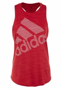 Červený sportovní top s racerback designem, na němž se nachází velké bílé logo Adidas se šikmými pruhy, vyrobený z texturovaného, lehkého materiálu.