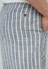 Gestreepte stofbroek in marineblauw en wit, met een gestructureerde weef, een logo-label en zijzakken voor praktisch gebruik.