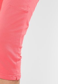 Koralové capri kalhoty s hladkou texturou, obsahující boční kapsu a ohrnutý lem, vyrobené z lehkého bavlněného materiálu.