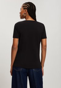 Czarna koszulka z krótkim rękawem, wykonana z gładkiego materiału. Charakteryzuje się luźnym krojem i okrągłym dekoltem. W połączeniu z ciemnoniebieskimi spodniami dżinsowymi.