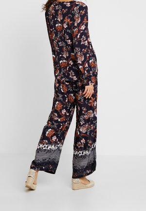 Bluse mit floralem Muster in Marineblau und langen Ärmeln, kombiniert mit weit geschnittenen Hosen mit gestreiftem Saum. Dazu beigefügte beigefarbene Espadrilles.