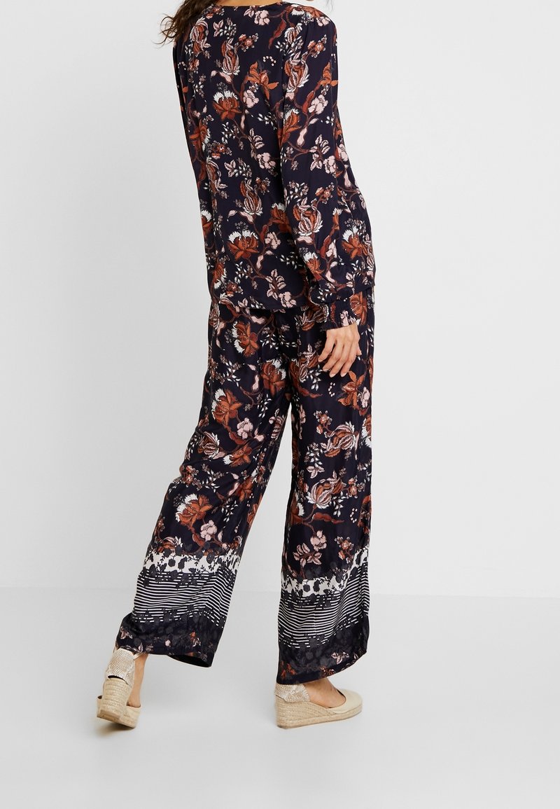Bluse mit floralem Muster in Marineblau und langen Ärmeln, kombiniert mit weit geschnittenen Hosen mit gestreiftem Saum. Dazu beigefügte beigefarbene Espadrilles.