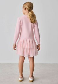 Ružové sveterové šaty s volánovým tylovým lemom, mäkkou textúrou, dlhými rukávmi a v kombinácii s bielymi topánkami s ružovým detailom na zadnej strane.