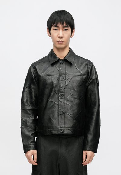 Veste en cuir noir avec un design texturé, fermeture à boutons et col pointu ; présente des plis subtils pour un look unique.