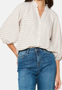 Ljust färgad, texturerad blus med mandarinkrage, subtil randig design i blått och rosa, samt puffärmar. Kombinerad med blå jeans.