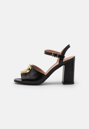 Sandales à talons hauts noires en cuir avec un accent logo doré, bout ouvert et sangle de cheville avec détail de boucle. Design de talon carré.