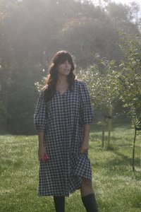 Abito a scacchi grigio e bianco con chiusura a bottoni, maniche ampie e spacco laterale, abbinato a stivali neri fino al ginocchio in un contesto all'aperto con erba.