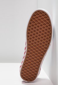 Ruitvormige rood-witte canvas sneaker zool met een bruine rubberen patroon, met een gestructureerde grip en witte rand.