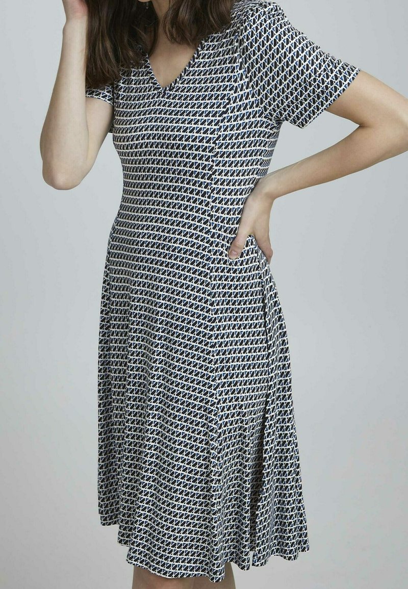 Klassisk klänning med V-ringning och korta ärmar, med ett marinblått och vitt geometriskt mönster, tillverkad av ett mjukt och stretchigt material, i A-linjeform.