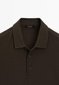 Mörkbrun polo skjorta med en strukturerad tyg, en knappkrage och tre bruna knappar vid halsen. Etikett med texten "Massimo Dutti."
