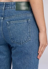 Jeans z denimu s klasickým designem v světle modré barvě. Obsahují zelenou koženou nášivku a zadní kapsu s vyšívanými detaily.